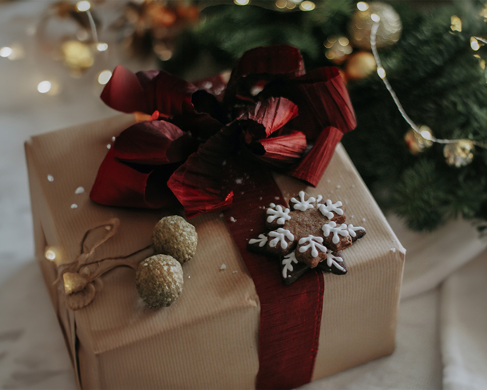 Božićni poklon umotan u papir, vezan mašnom i ukrašen kolačićem.