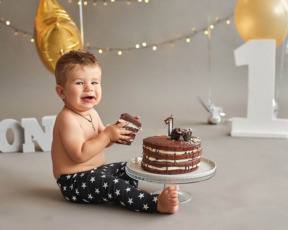 Jednogodišnji dečak u rukama drži komad čokoladne torte da proslavi svoj rođendan