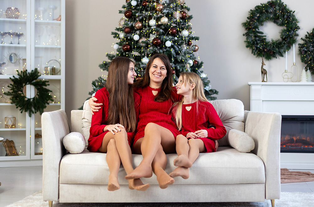 Mama i njene ćerke u crvenim haljinama provode praznično vreme zajedno pored jelke.