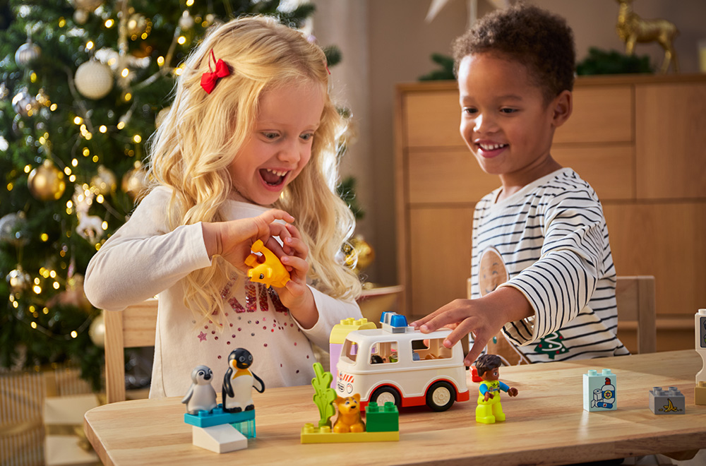 Dvoje dece se igraju sa LEGO kockicama ispod božićne jelke.