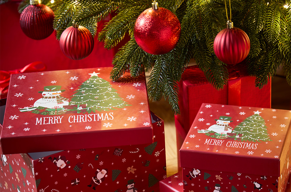 Poklon kutije sa božićnim motivima pored božićne jelke.