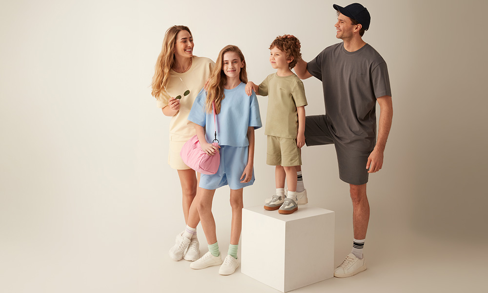 Porodica u pastelnim odevnim kombinacijama pozira zajedno na svetloj pozadini.